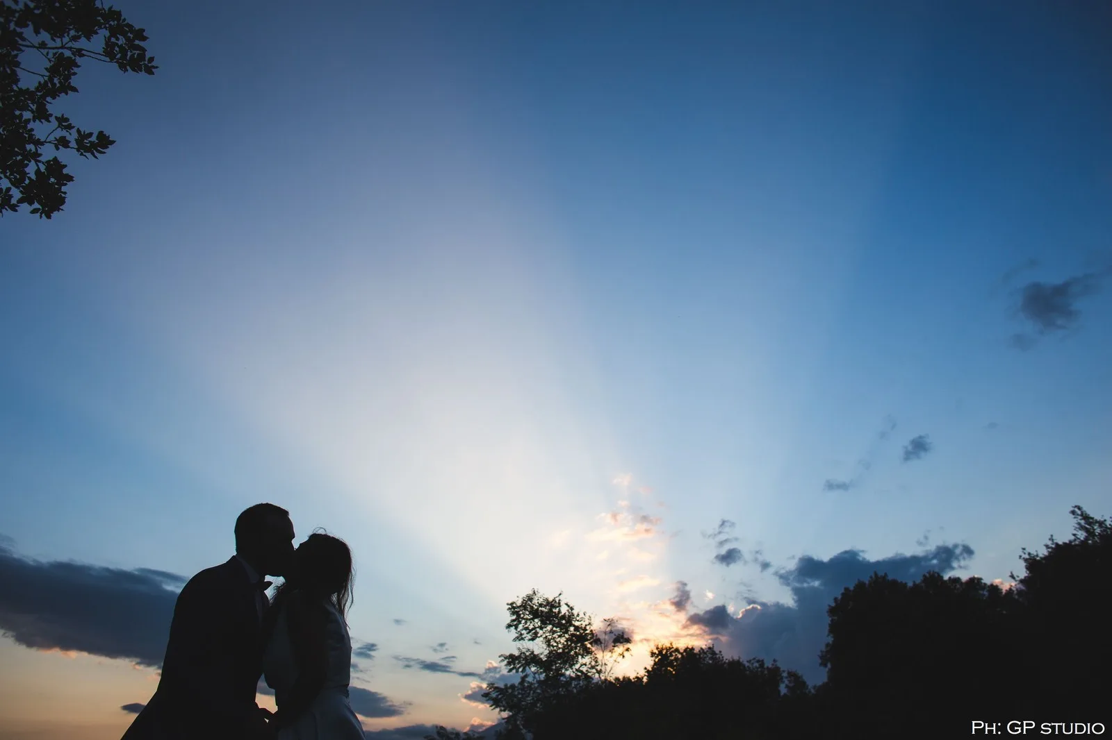 Cielo al tramonto con raggi di sole tra le nuvole e silhouette di una sposa