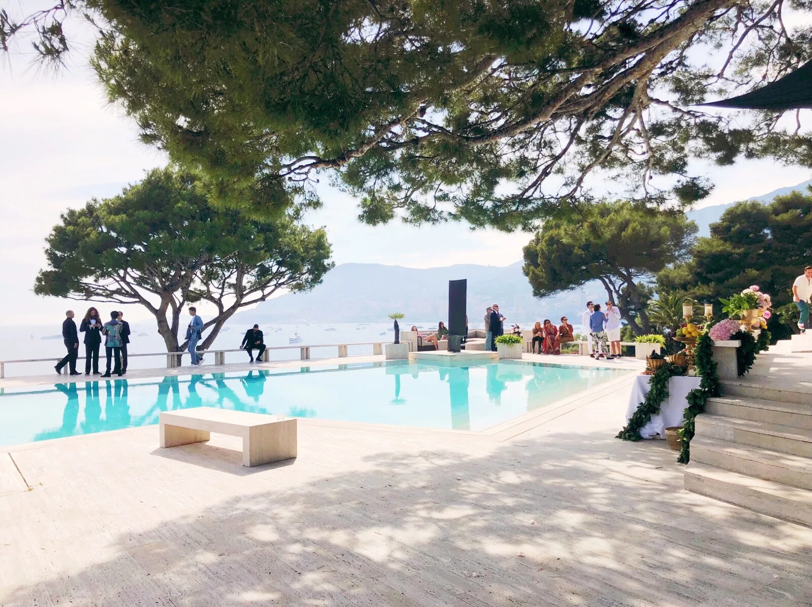 Piscina a sfioro sul mare con ospiti rilassati all'ombra dei pini