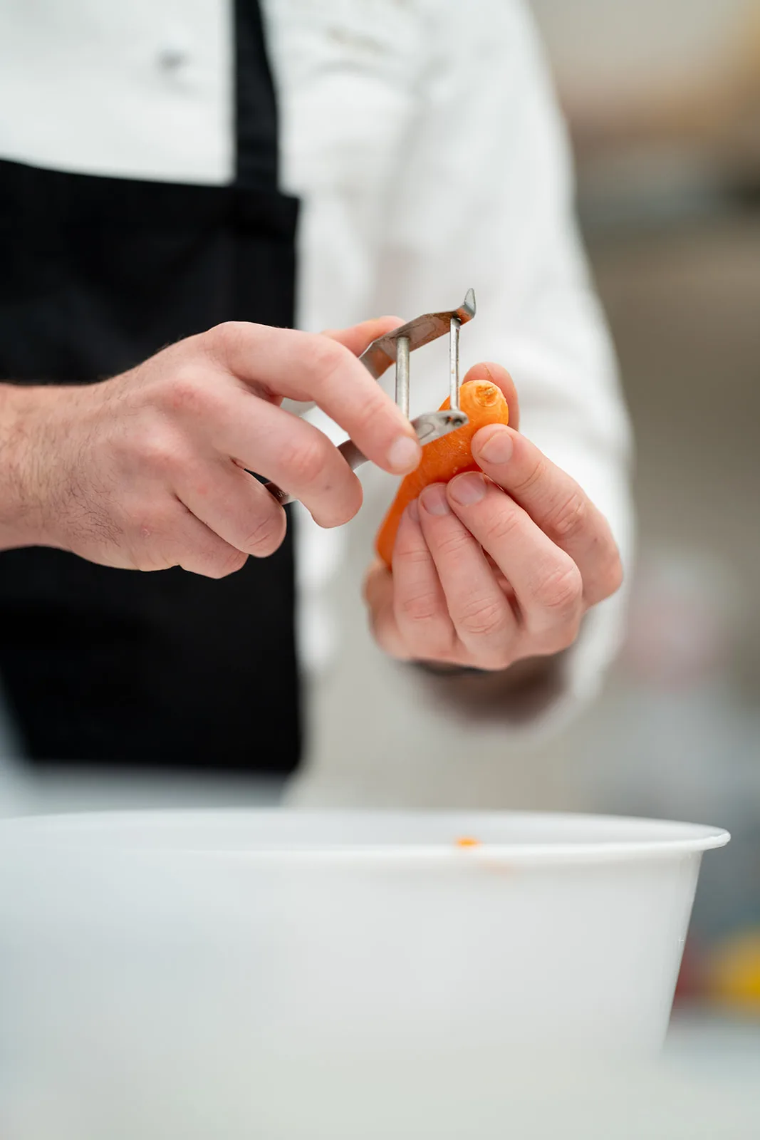 Lo chef pela una carota a mano con il pelapatate in cucina