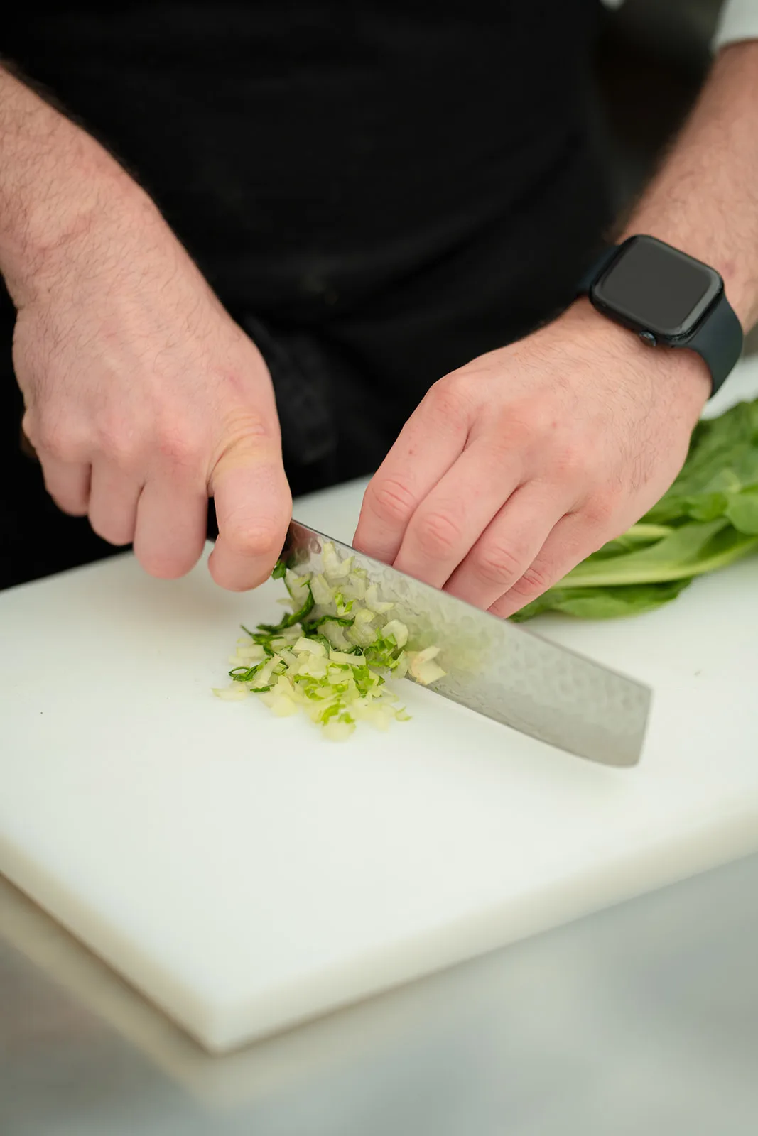 Lo chef trita finemente cipollotto fresco sul tagliere bianco