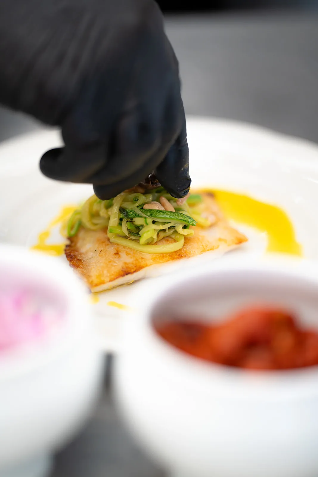 Zucchine julienne adagiate su pesce dorato da mani guantate