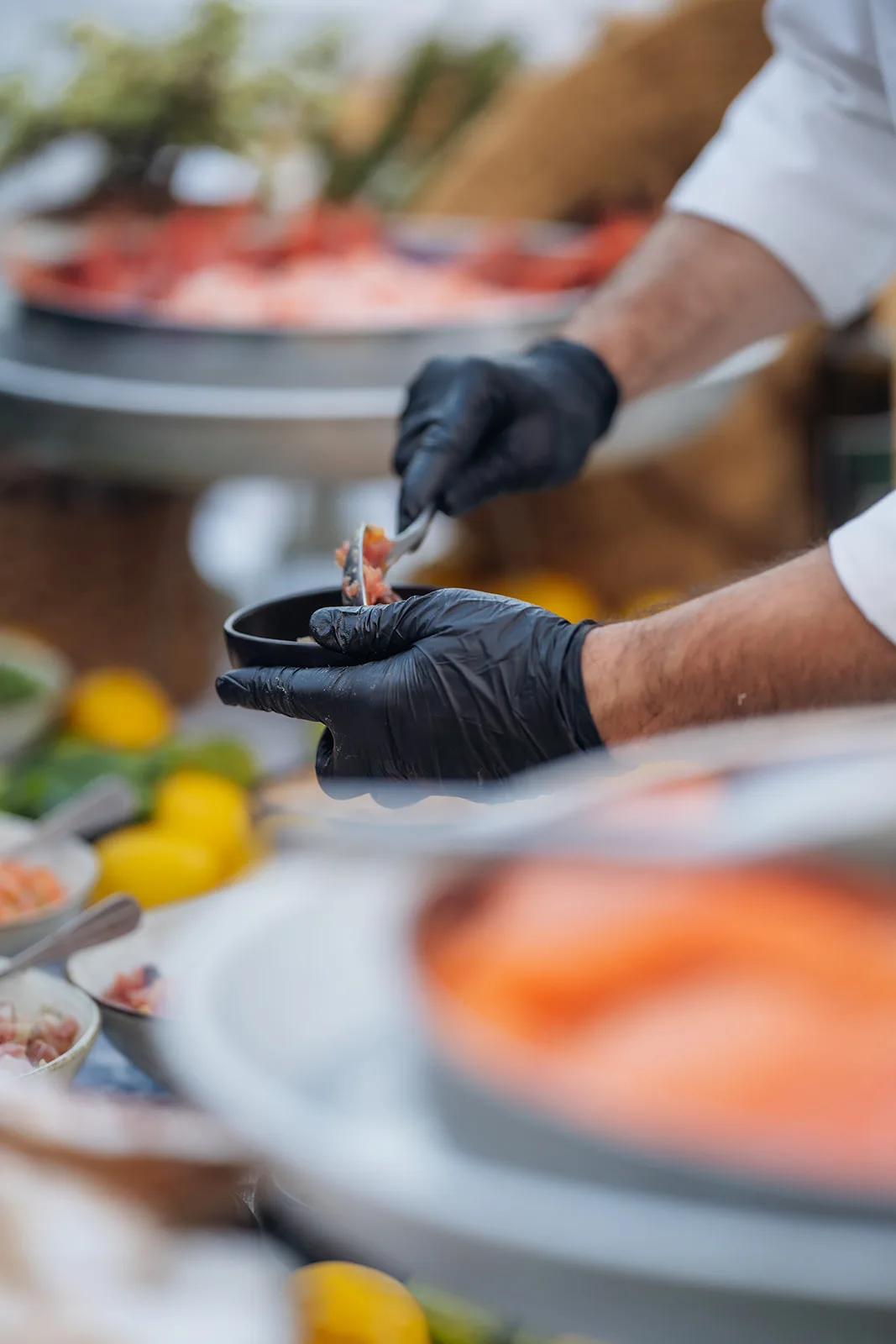 cuoco in guanti neri compone un assaggio di crudo di pesce al buffet