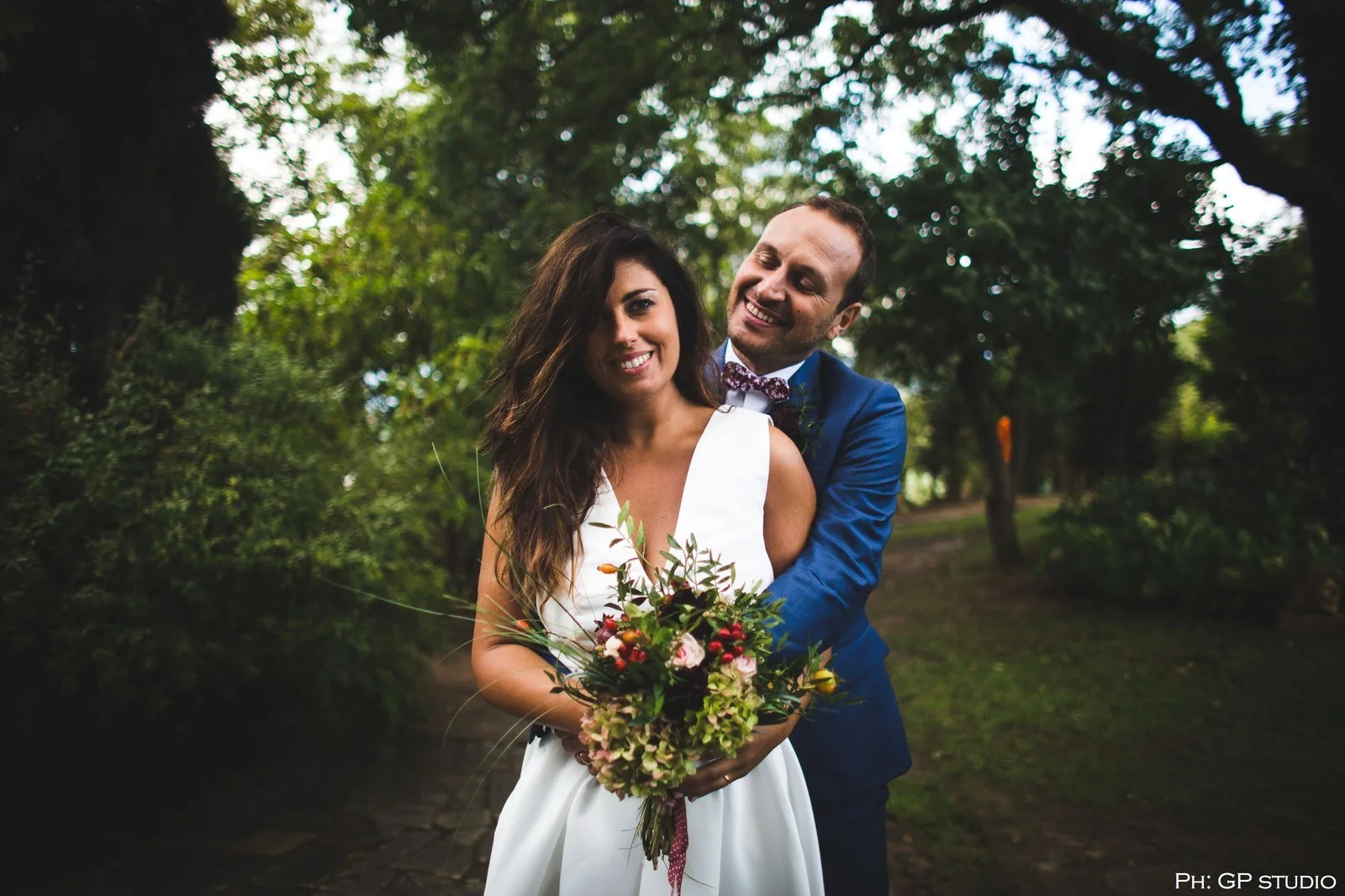 sposi sorridenti abbracciati nel verde con bouquet autunnale