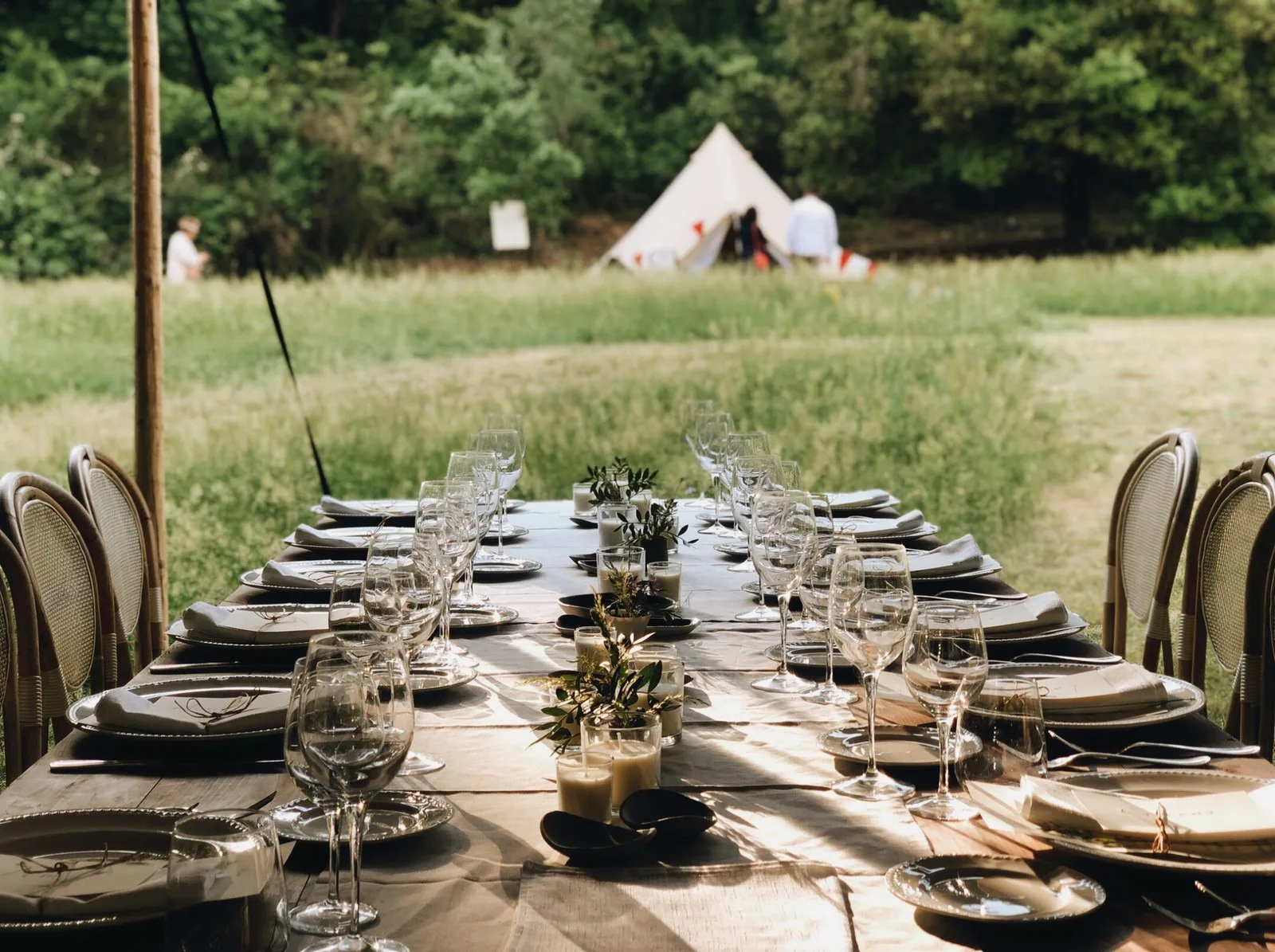 Tavolo rustico apparecchiato tra i prati con tende glamping sullo sfondo
