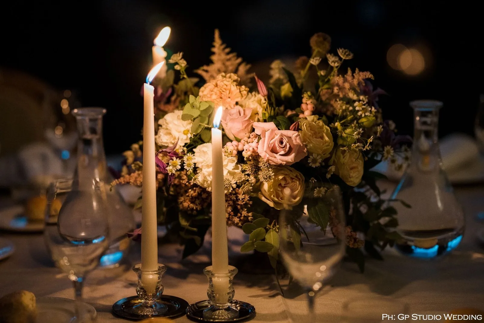 Candele accese tra rose e fiori in un centrotavola serale