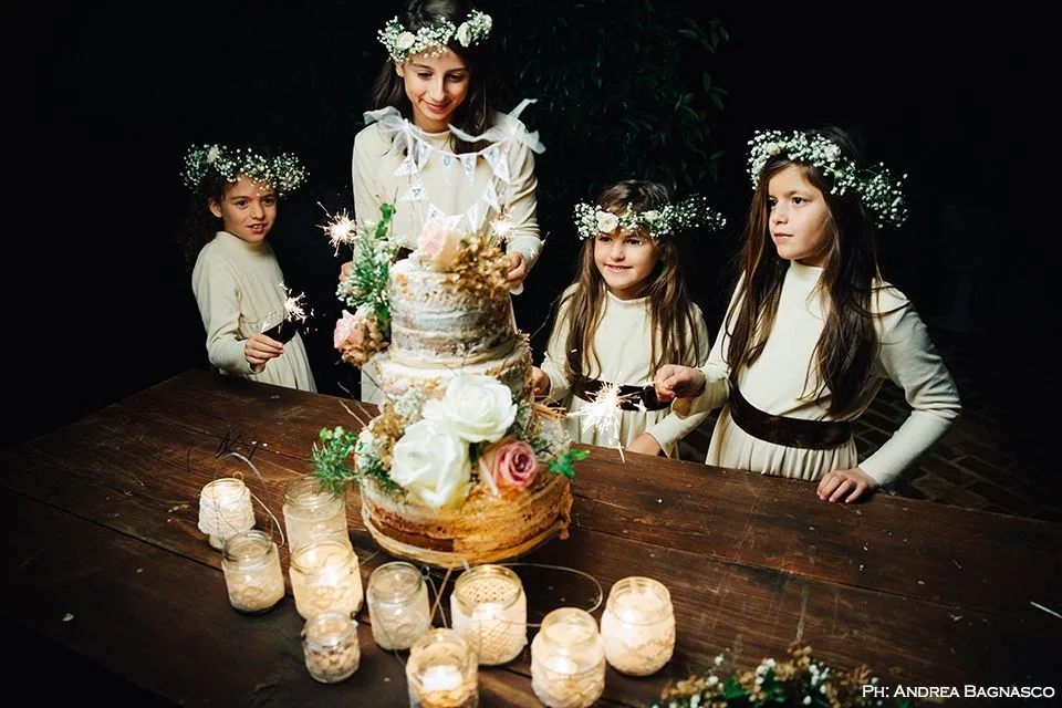 Bambine con corone di fiori attorno alla torta nuziale al buio