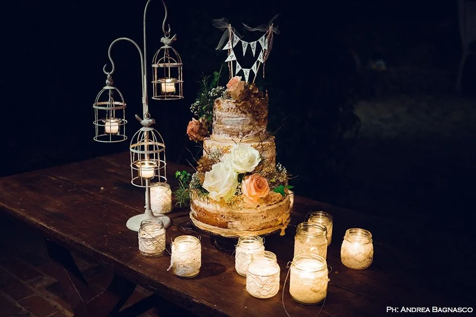 Torta nuziale rustica tra candele e lanterne su tavolo in legno
