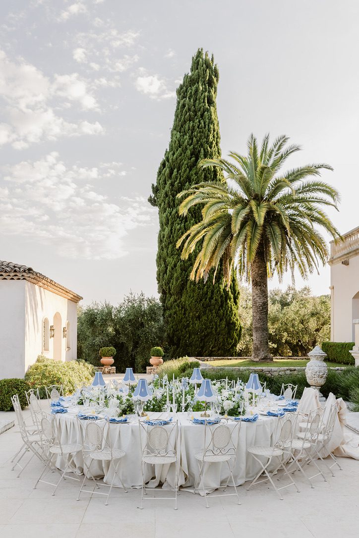 Tavolo imperiale con dettagli blu e bianco sotto un alto cipresso e una palma