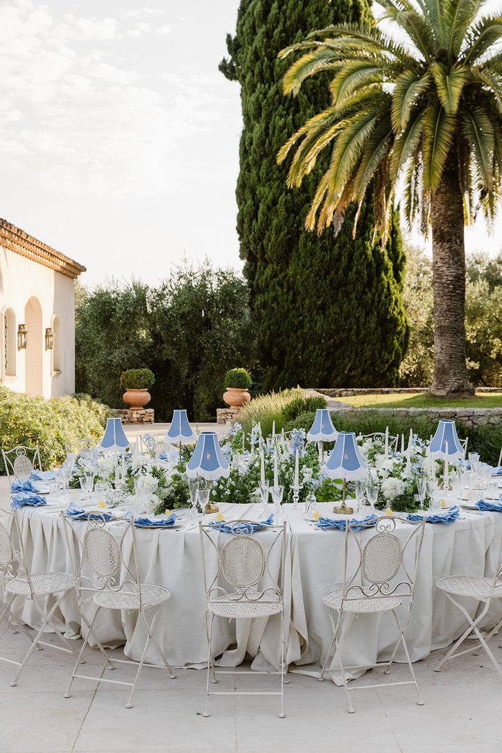 Tavolo imperiale completo con paralumi blu, fiori bianchi e una palma sullo sfondo