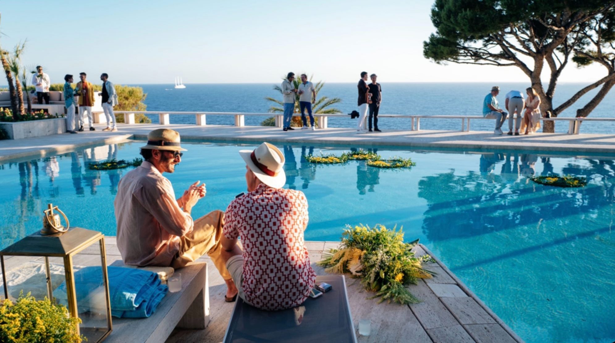 due ospiti seduti bordo piscina osservano il mare al tramonto